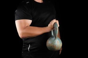 adult strong athlete in black clothes holding an iron kettlebell on his outstretched arms photo