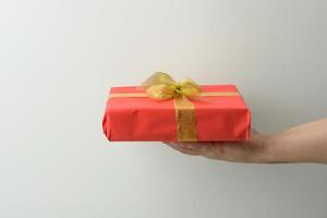 mano femenina sostiene una caja de regalo roja sobre un fondo gris, concepto de feliz cumpleaños foto