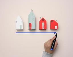 A miniature wooden house and a woman's hand draws a graph with growing indicators. photo