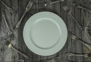 plato vacío sobre una superficie de madera gris, alrededor de muchos tenedores de hierro foto