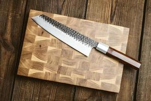 metal kitchen knife and wooden cutting board on a table made of brown wooden boards photo