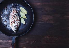 Carp fish in spices on a black cast-iron frying pan photo