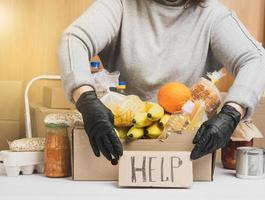 woman in a gray sweater is packing food in a cardboard box, the concept of assistance and volunteerin photo
