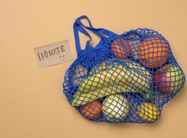 ripe fresh fruits in a textile string bag on a brown background, top view photo