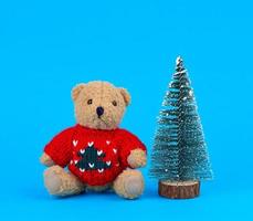 pequeño oso de peluche en un suéter rojo de navidad y un árbol decorativo foto