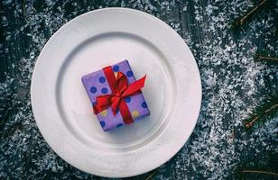 Packed gift with a red ribbon on a white plate photo