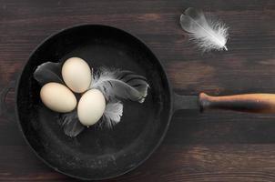 Three raw chicken eggs in a black cast-iron frying pan photo