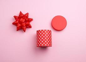 round red cardboard box in white polka dots on top of a bow on a pink background photo