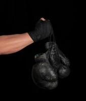 el brazo envuelto en una venda deportiva elástica negra sostiene un par de guantes de boxeo de cuero antiguos foto