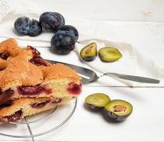 slices of biscuit plum cake on a white wooden board and fresh fruits photo