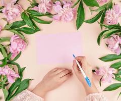 mano femenina sostiene un bolígrafo blanco sobre una hoja de papel rosa vacía foto