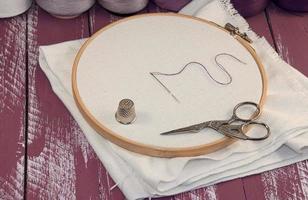 White fabric in the wooden embroidery frame with a set of threads in coils for needlework photo