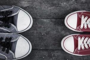 Two pairs of well-worn sneakers on a wooden surface photo