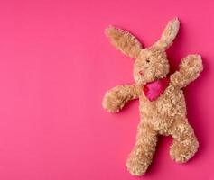 toy brown plush hare lies on a pink background photo