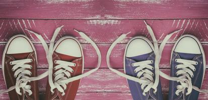 Two pairs of worn sneakers on a pink old wooden surface photo