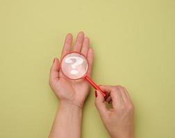 female hand holds a plastic magnifying glass and question marks on a green background. The concept of finding an answer to questions photo