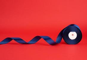 spool of twisted dark blue silk shiny ribbon on a red background photo