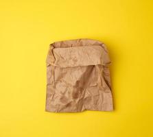 open brown paper bag for food packaging with greasy stains on a yellow background photo