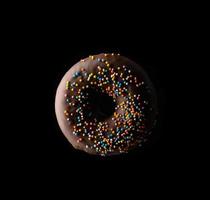 los donuts de chocolate con chispas multicolores levitan sobre un fondo negro foto