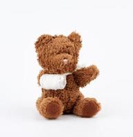 brown teddy bear with rewound white bandage paw on a white background photo