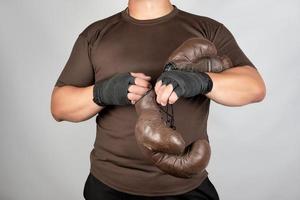 young man stands and puts on his hands very old vintage brown boxing gloves photo