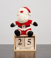santa claus in red hat, table wooden calendar with the date december 25 photo