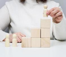 una mujer con un suéter blanco pone una figura de madera en el podio. el concepto de búsqueda de empleados, promoción profesional. empleado talentoso foto