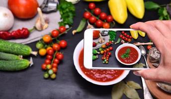 Female hand with smartphone in hand photographs soup gazpacho