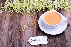 cup of coffee on a saucer, next to a bouquet of white lilies of the valley photo