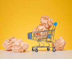 Crumpled balls of paper in a miniature shopping cart on a yellow background. New ideas and innovations photo