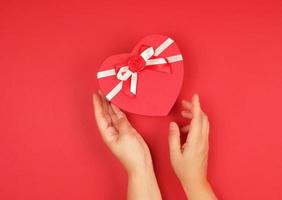 two hands hold a paper closed red box in the shape of a heart photo