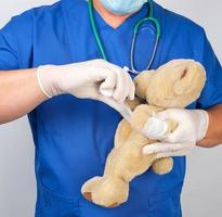 doctor in blue uniform bandages white medical bandage paw brown teddy bear photo