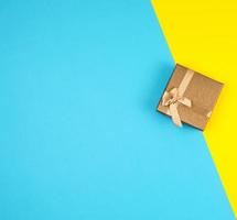 caja de regalo dorada cerrada con un arco sobre un fondo amarillo azul foto