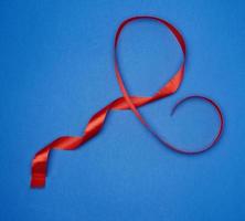 red silk thin ribbon twisted on a blue background, trendy classic color photo