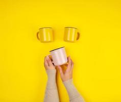 tazas de cerámica y manos femeninas sobre un fondo amarillo foto