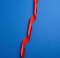 red silk thin ribbon twisted on a blue background photo