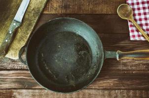 Black cast-iron frying pan with a kitchen board on the table photo