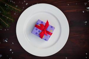 Packed gift with a red ribbon on a white plate photo