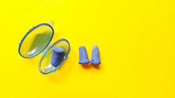 tapones para los oídos de espuma azul suave en un recipiente de plástico y un par de tapones para los oídos sobre fondo amarillo foto