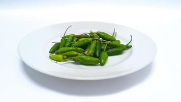 Cerca de chiles verdes crudos en un plato blanco aislado sobre fondo blanco. foto