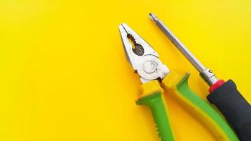 Screwdriver and pliers isolated on yellow background photo