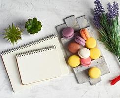 baked round multi-colored macarons on a wooden board, stack of spiral notebooks photo
