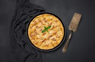 Round baked apple pie on a black table. View from above photo