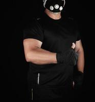 athlete in black uniform, training mask and hands wrapped in black bandage stands photo