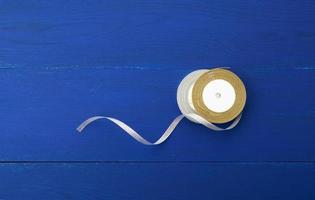 two round bobbins with silver golden ribbon on a blue wooden background photo