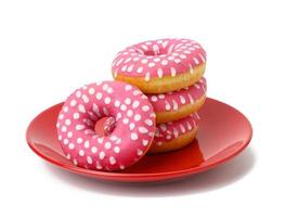 stack of baked donuts with pink frosting on a red round plate, food isolated on blue background photo