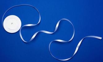 white silk thin ribbon twisted into a reel on a blue background photo