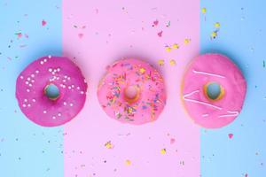 three round different sweet donuts with sprinkles on a pink-blue background photo