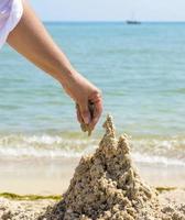 la mano construye un castillo de la arena mojada del mar foto