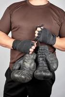 athlete in brown clothes holds very old vintage leather black boxing gloves photo